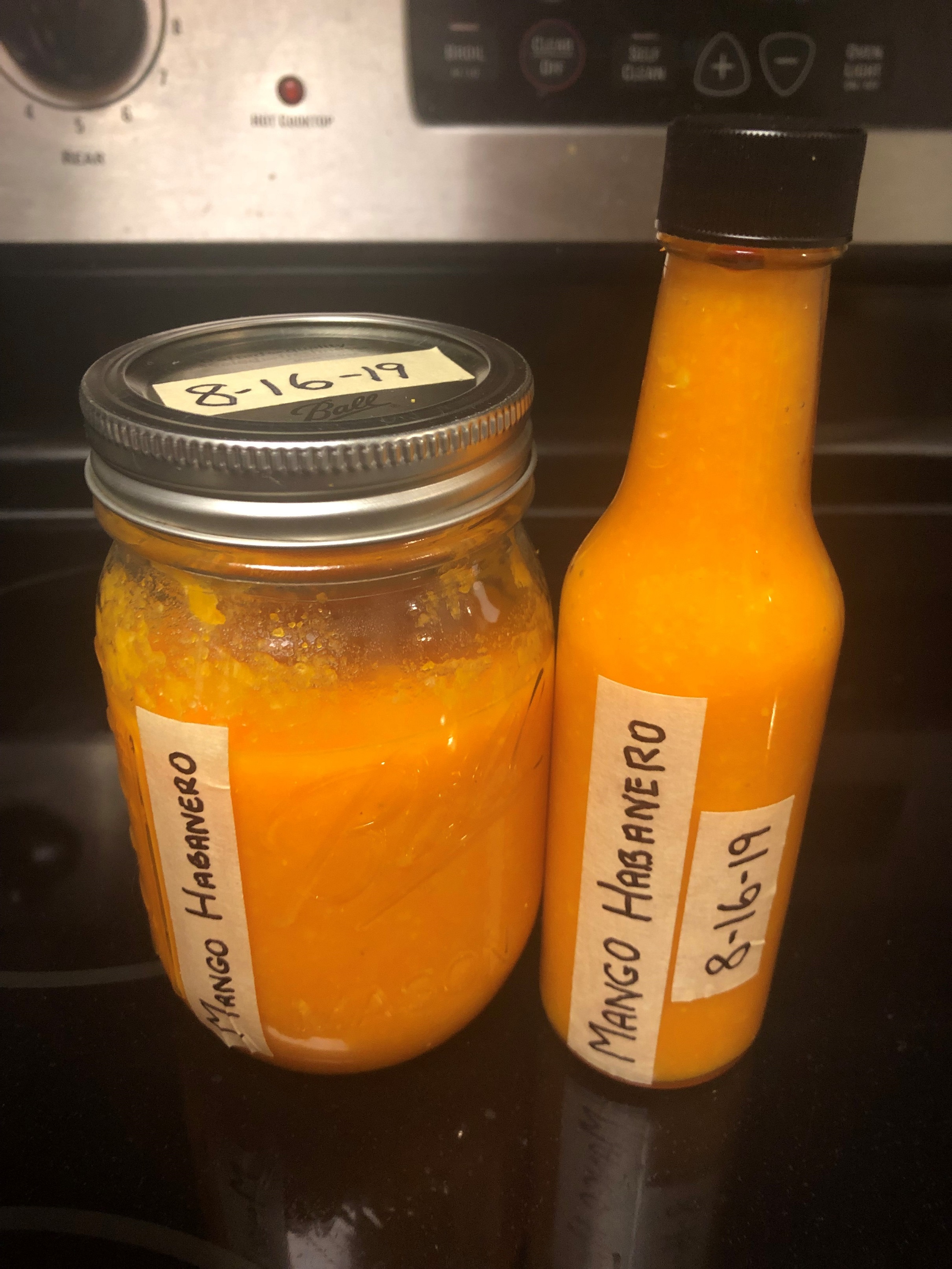 Bottled and labeled sauce on stove in a hot sauce bottle and mason jar