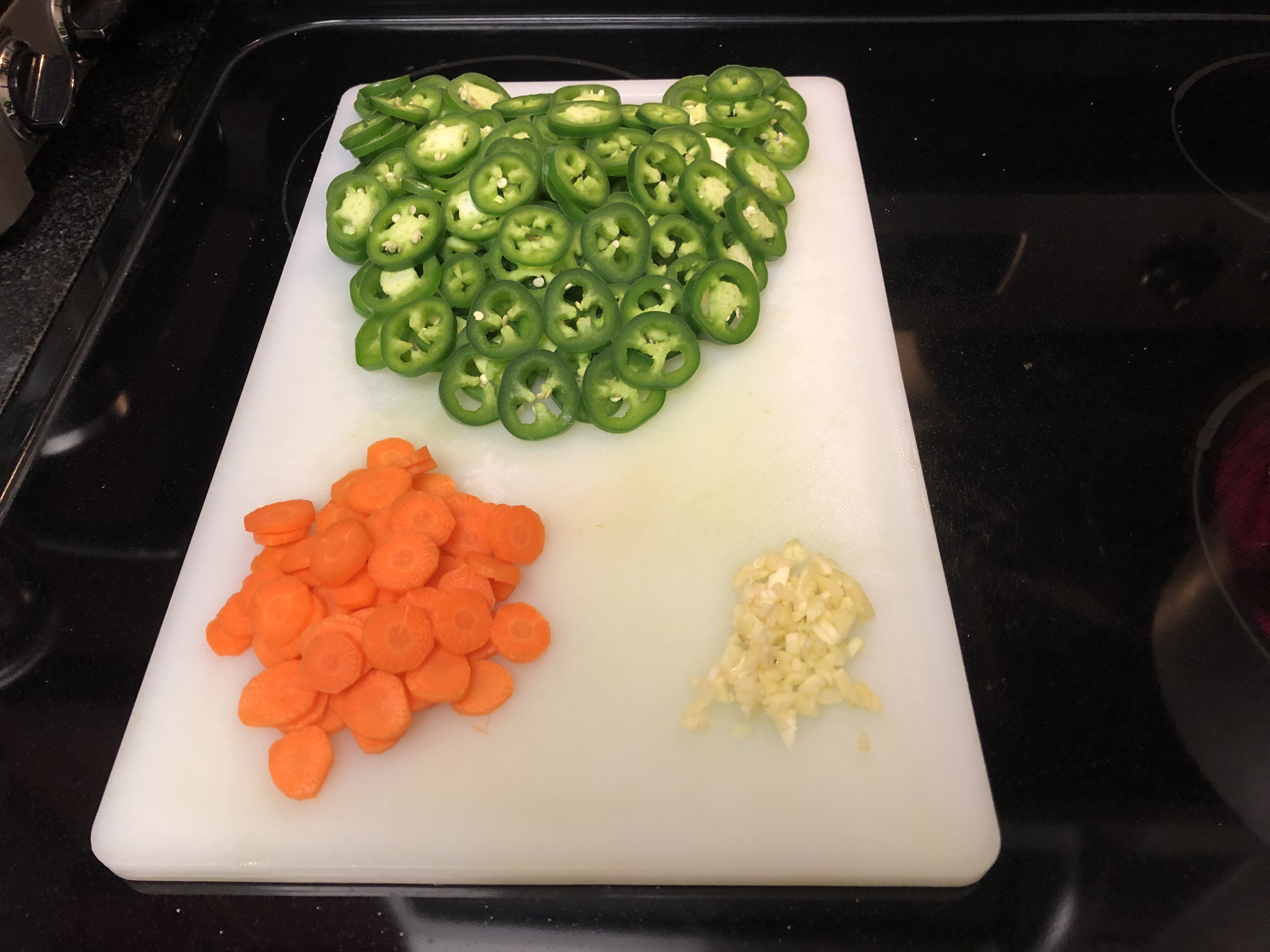 Cutting board showing prepared ingredients with sliced jalapenos and carrots and smashed garlic