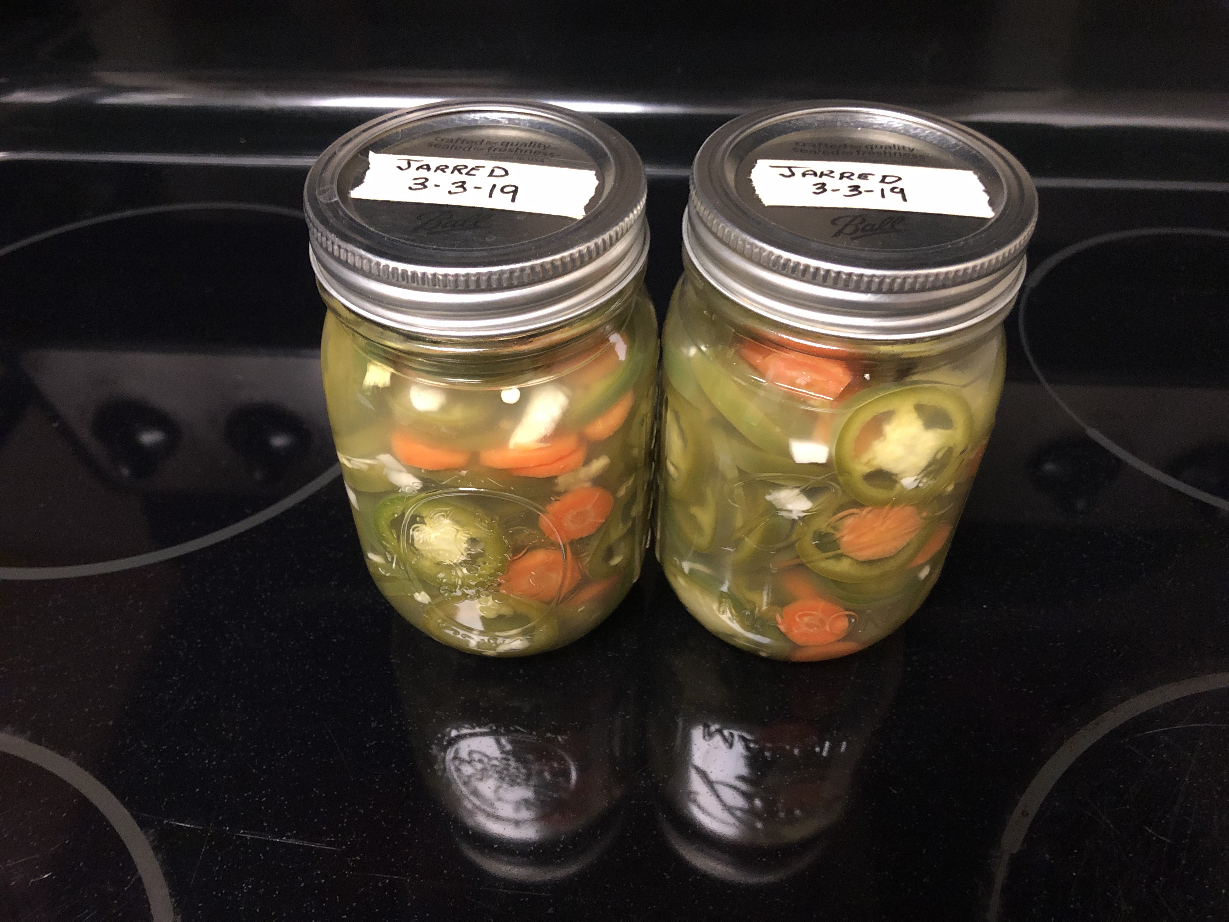 Ingredients and brine in mason jars with labeled tape on lid showing jarred date
